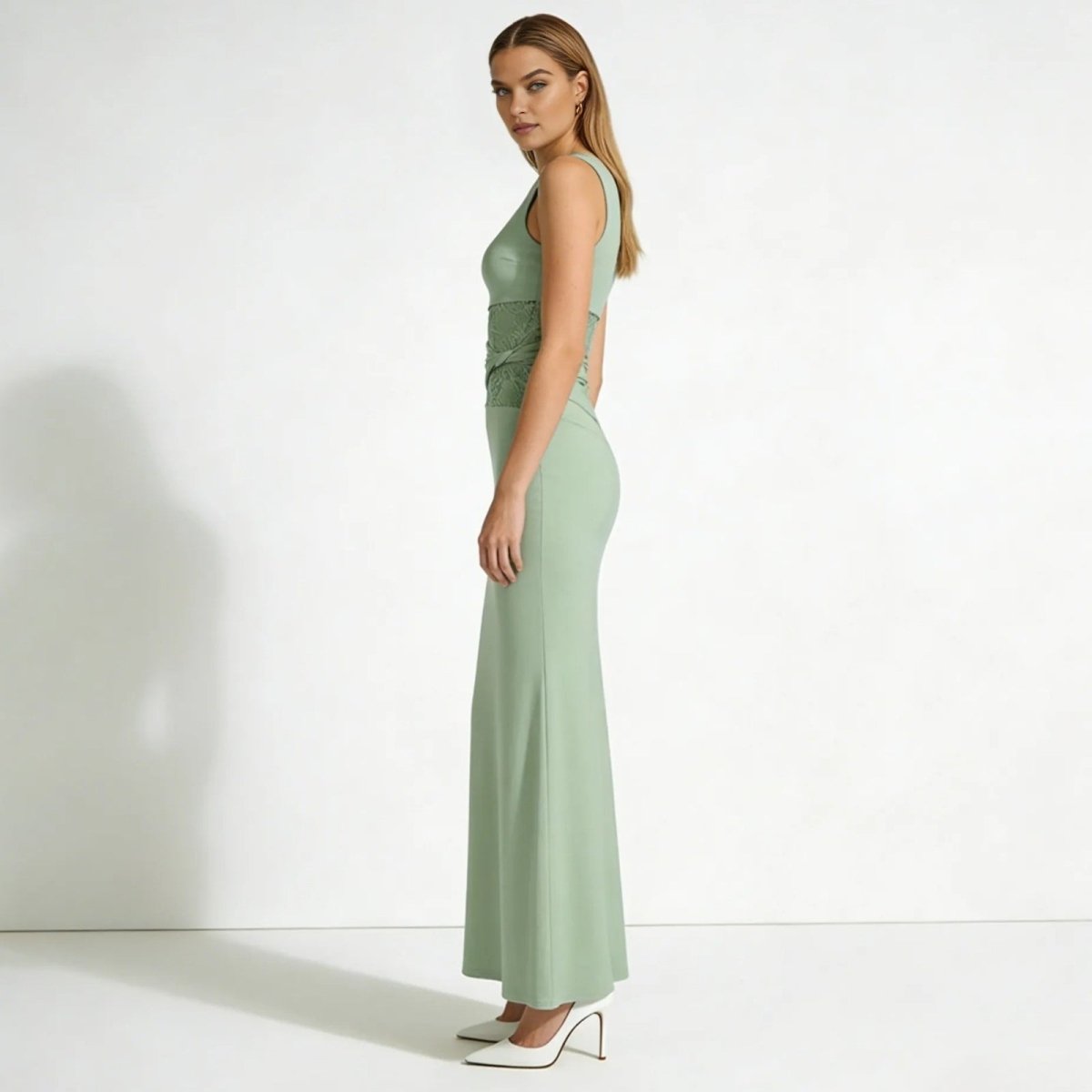 Side profile of a woman in a sage green sleeveless evening gown showing the slim column silhouette and criss-cross lace waist.
