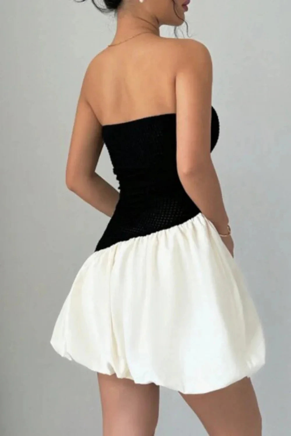 Model wearing Kouvr Fashion strapless black and white bubble hem mini dress against background