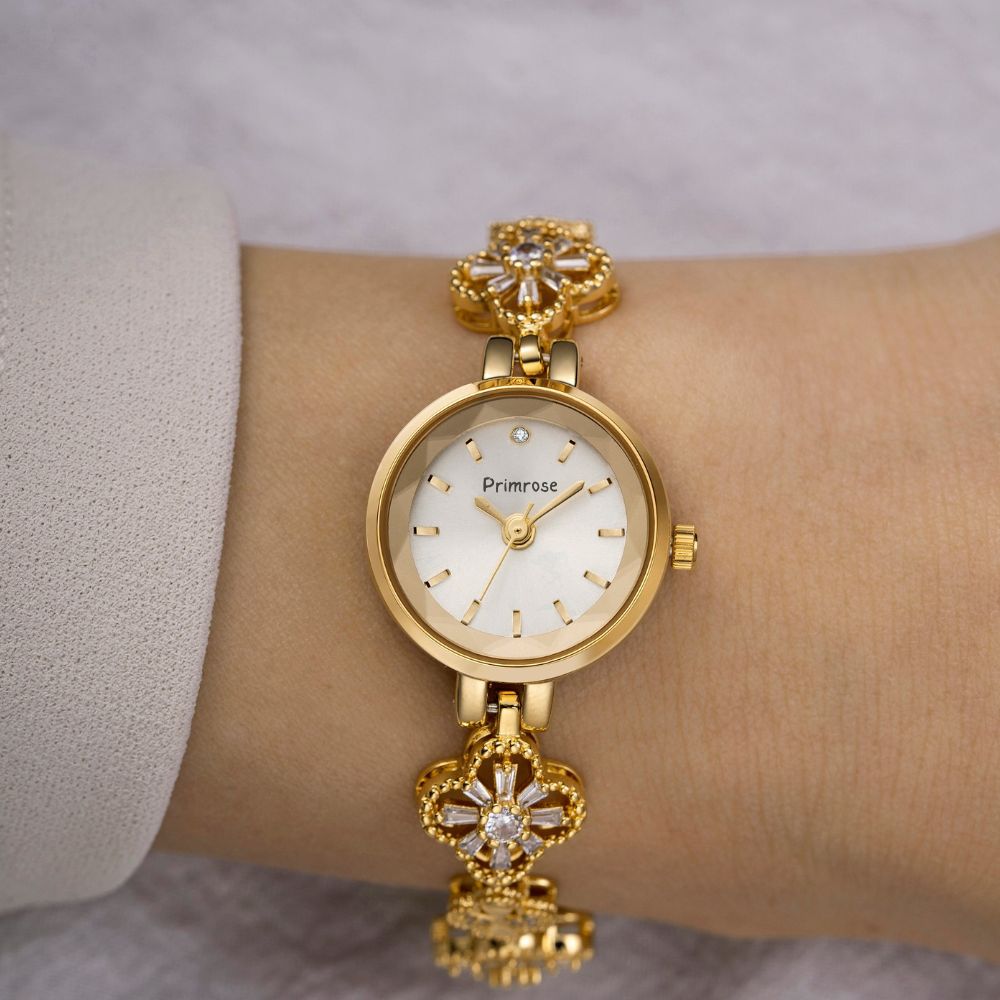 Gold Kouvr wristwatch with floral designs on a wrist against a neutral background