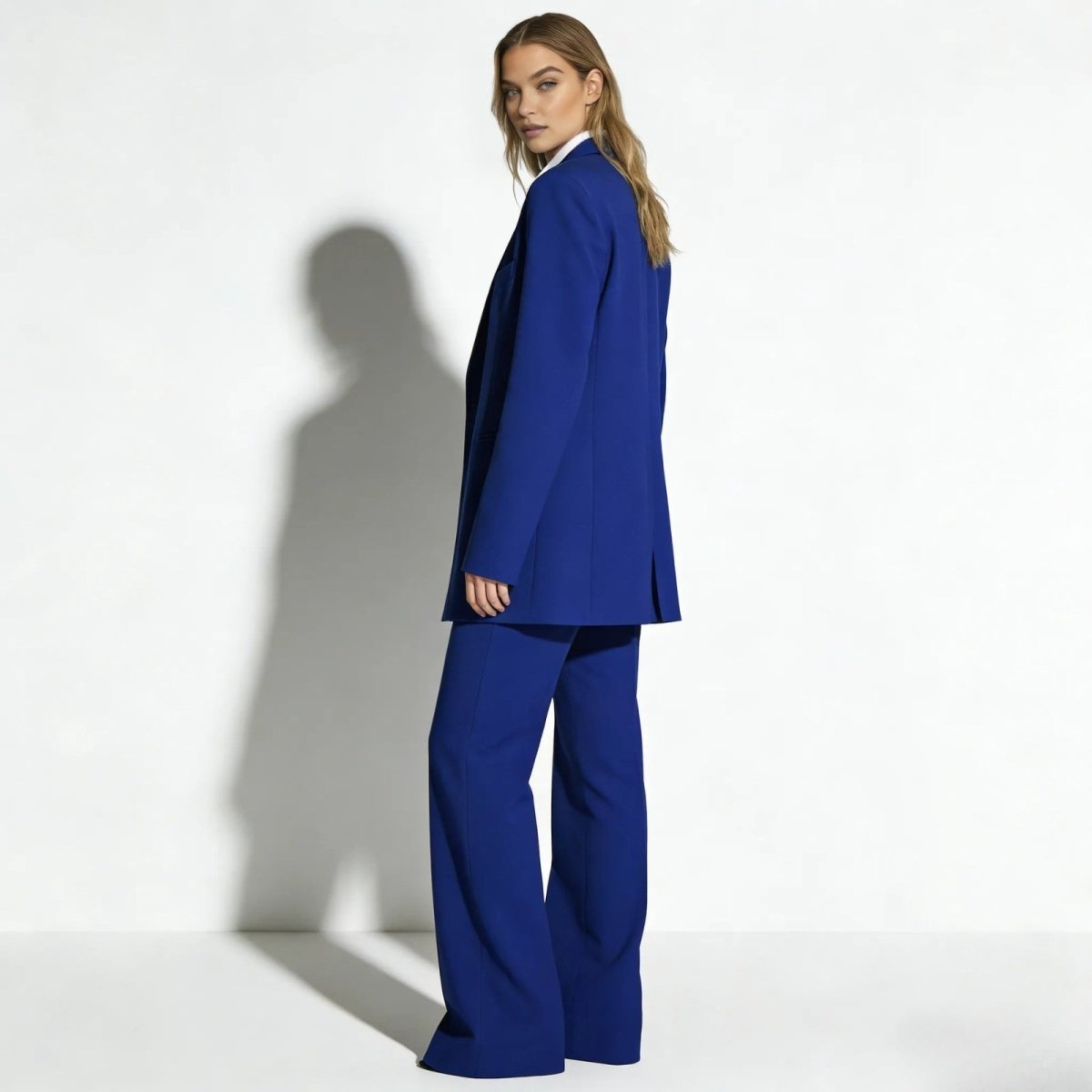 Side profile view of a woman in a royal blue luxury suit from Kouvr Fashion, highlighting the longline fit of the blazer and the drape of the wide-leg pants.
