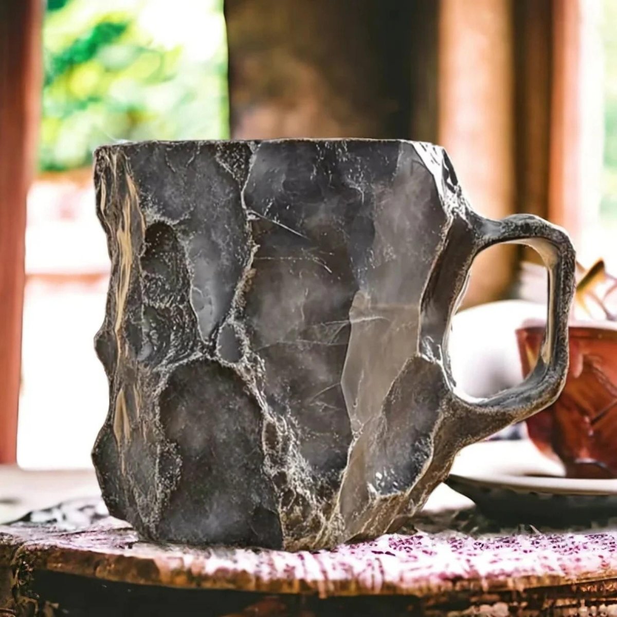 A large handcrafted stone coffee mug with a rugged black texture sitting on a rustic wooden table indoors.