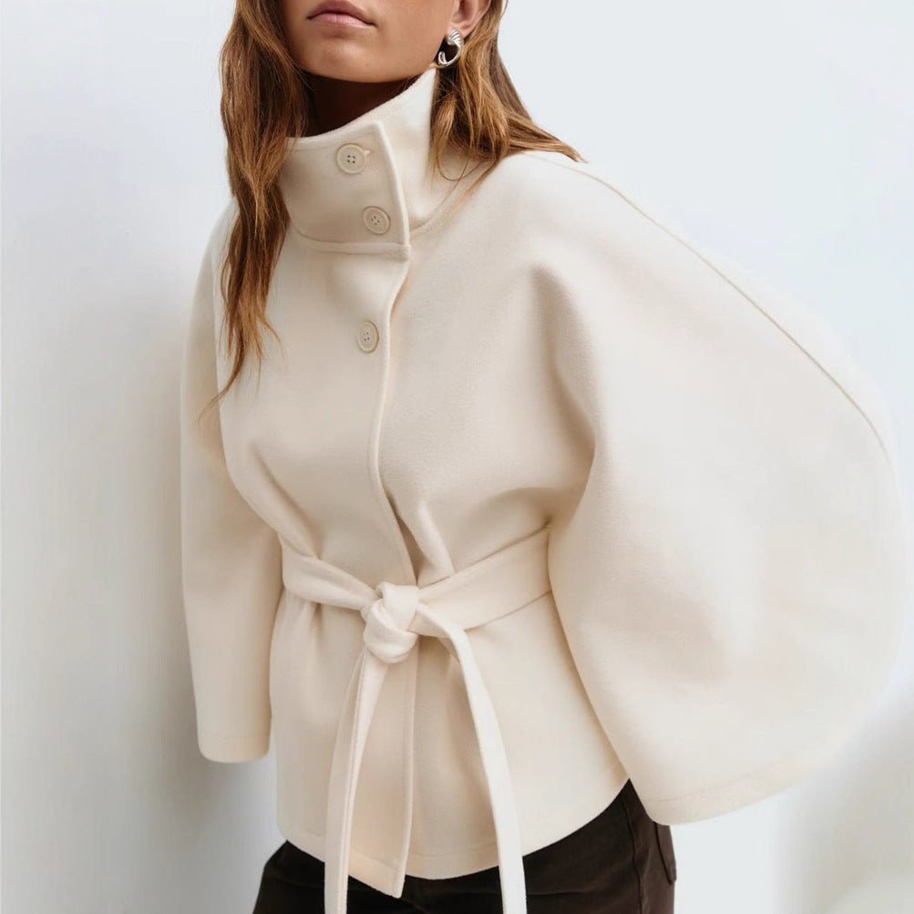 Model wearing the Kouvr Jannah Wool Cape Jacket in White, featuring a high funnel neck and tie-waist belt." For the back view