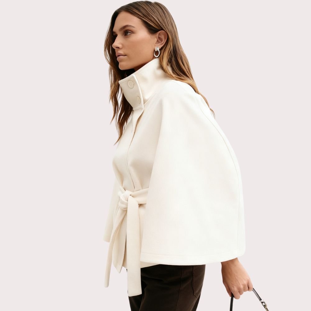 Model facing forward wears the Kouvr Jaye white wool belted cape coat with a high funnel neck and wide kimono sleeves