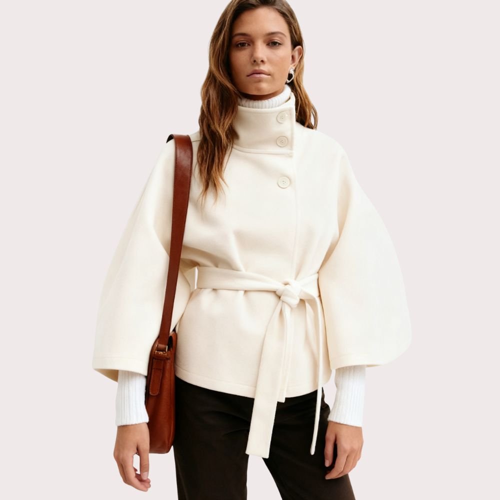 Model facing forward wears the Kouvr Jaye white wool belted cape coat with a high funnel neck and wide kimono sleeves