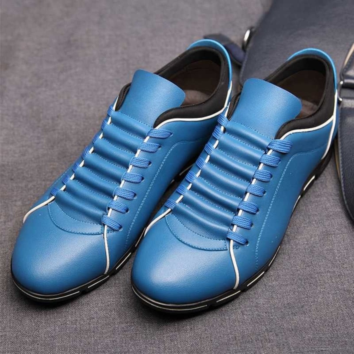A pair of vibrant blue leather Kouvr Jimmy men's sneakers with black and white accents, presented on a grey surface.