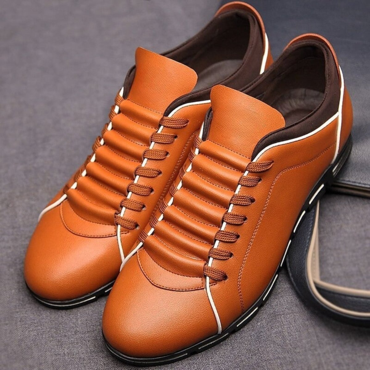 A front-angle view of a pair of orange leather Kouvr Jimmy men's dress sneakers, highlighting the clean lines and white lacing.
