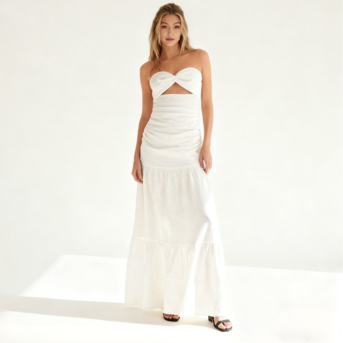 Woman wearing a strapless white Kouvr dress with a cutout design on a white background