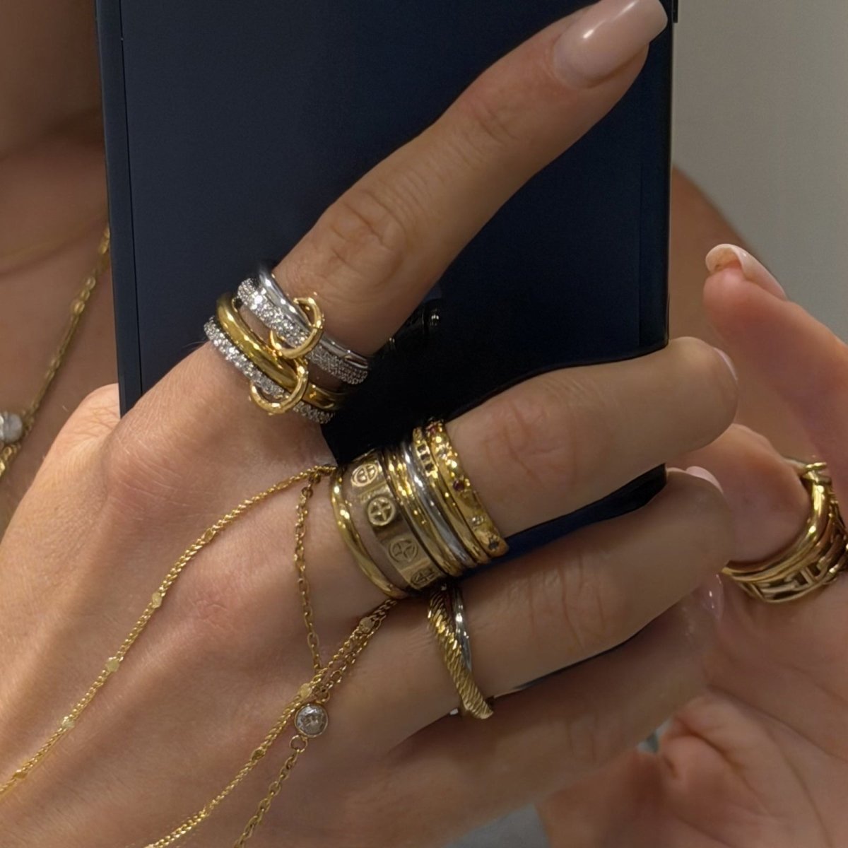 A woman styling the Kouvr Lirien two-tone gold rolling ring with other gold jewelry and holding a phone.