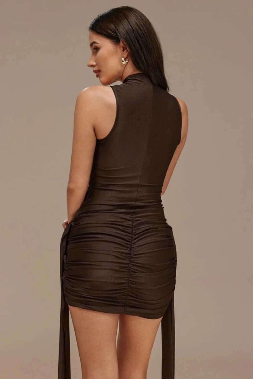 Model wears the Kouvr Madison high-neck sculptural bodycon mini dress in a rich espresso brown, featuring a draped skirt and long sashes