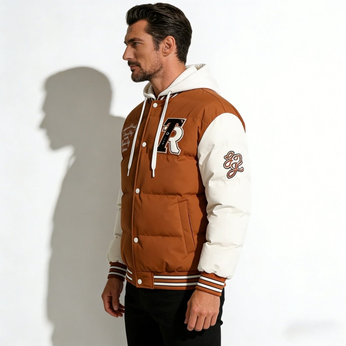 Side profile of a man wearing the Kouvr hooded bomber jacket, highlighting the contrast padded sleeves and athletic sleeve patches.