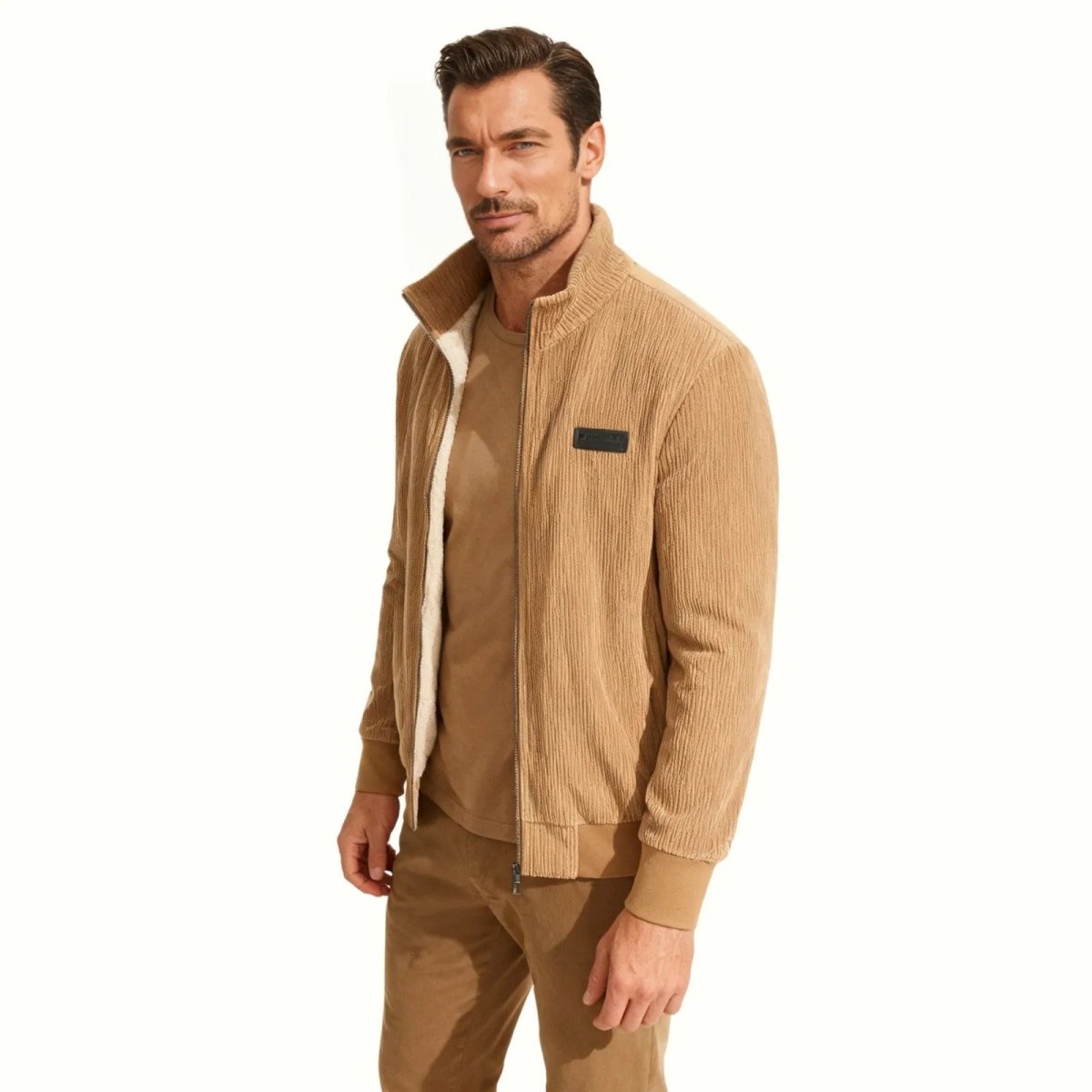 A male model shown from a three-quarter angle in the Kouvr beige corduroy bomber jacket, highlighting the jacket's fit and sherpa collar detail.