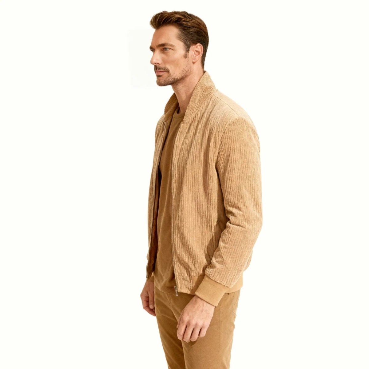 Side profile of a male model wearing the Kouvr beige corduroy bomber jacket, showing the jacket's silhouette and sleeve construction.