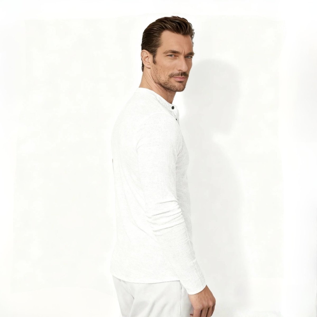 Man wearing the Kouvr men's white slub henley shirt looking over his shoulder, showing the side profile and modern fit.
