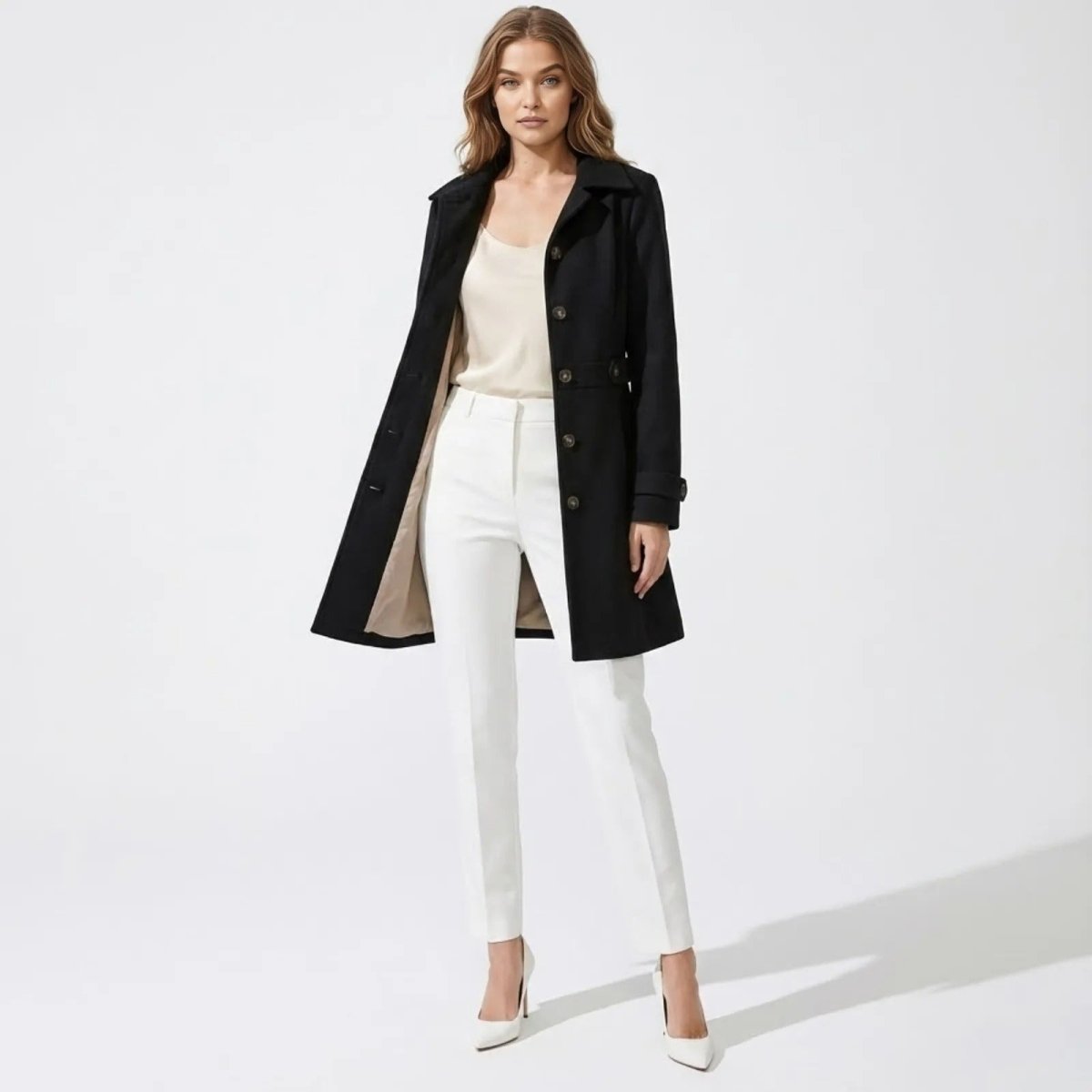Model wearing the Kouvr Priscilla tailored black wool coat open, styled with white trousers and a cream top against a white background.