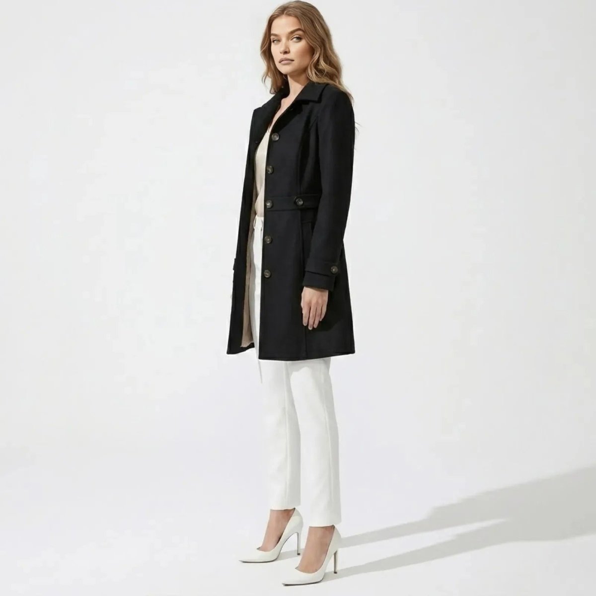 Side profile of a model wearing the Kouvr Priscilla single-breasted black wool coat, showcasing its tailored fit and knee-length cut.
