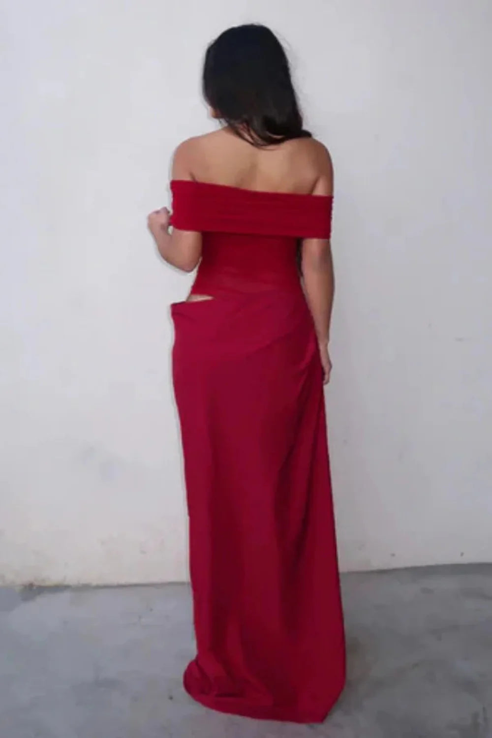 Front view of a woman wearing the Kouvr red off-shoulder formal gown with a sheer waist and hip cutout