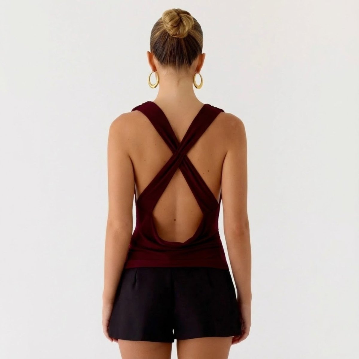 Side profile of a model in the Kouvr Rhea burgundy top, highlighting the drape of the fabric and the open-back silhouette.