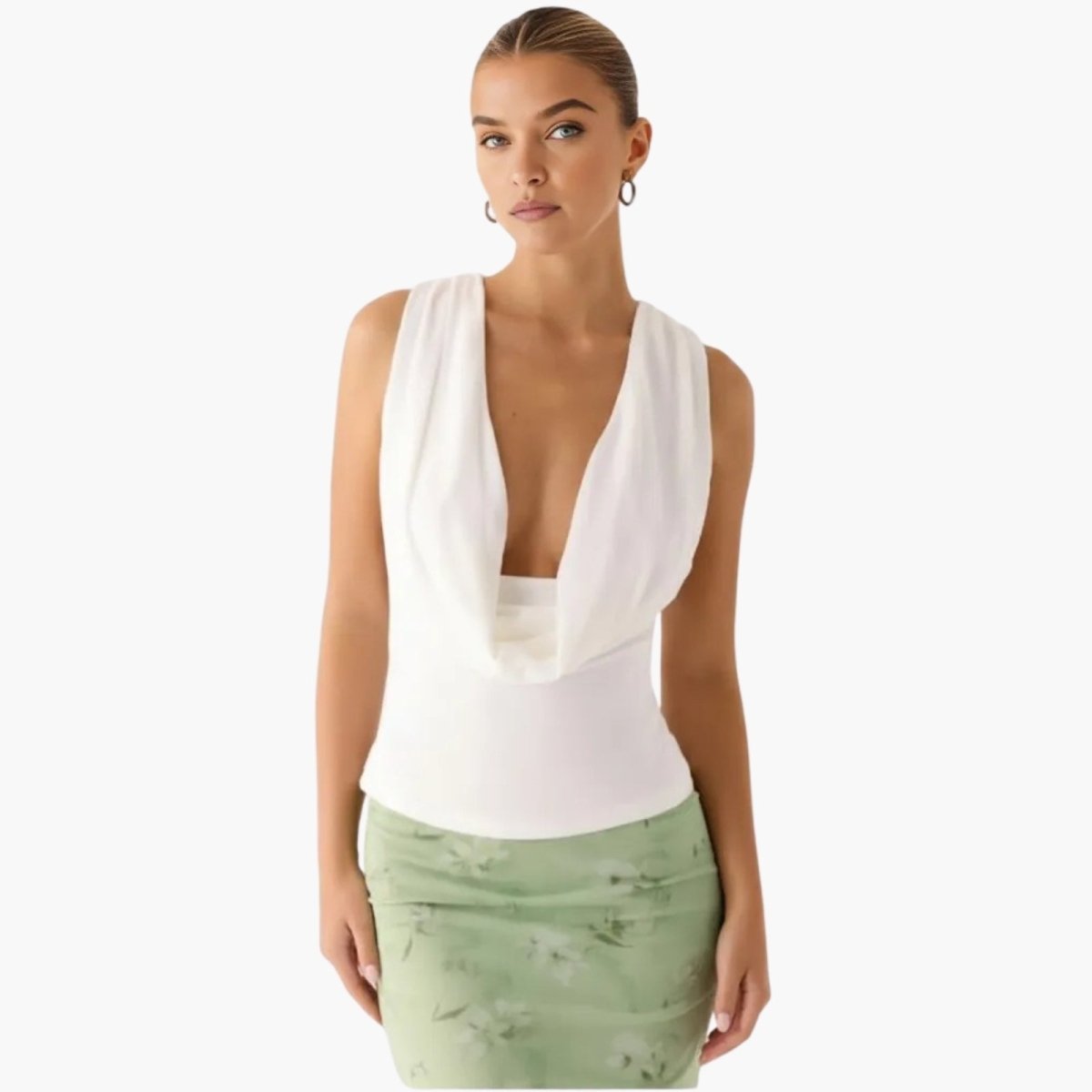 Model wearing the Kouvr Rhea white sleeveless cowl neck top paired with a light green floral skirt, showing the plunging draped neckline.