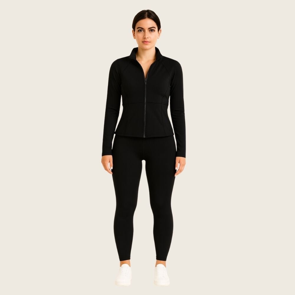 Woman wearing the black Kouvr Sculpting Athletic Jacket in a modern fitness studio.