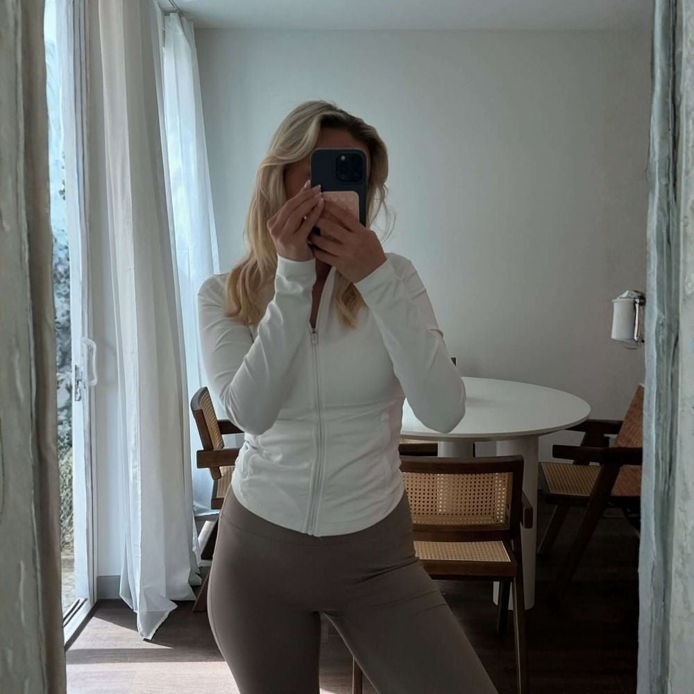 Model wearing the white Kouvr Sculpting Athletic Jacket in a modern fitness studio.