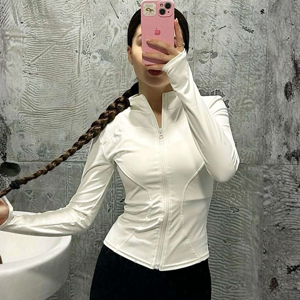 Model wearing the white Kouvr Sculpting Athletic Jacket in a modern fitness studio.