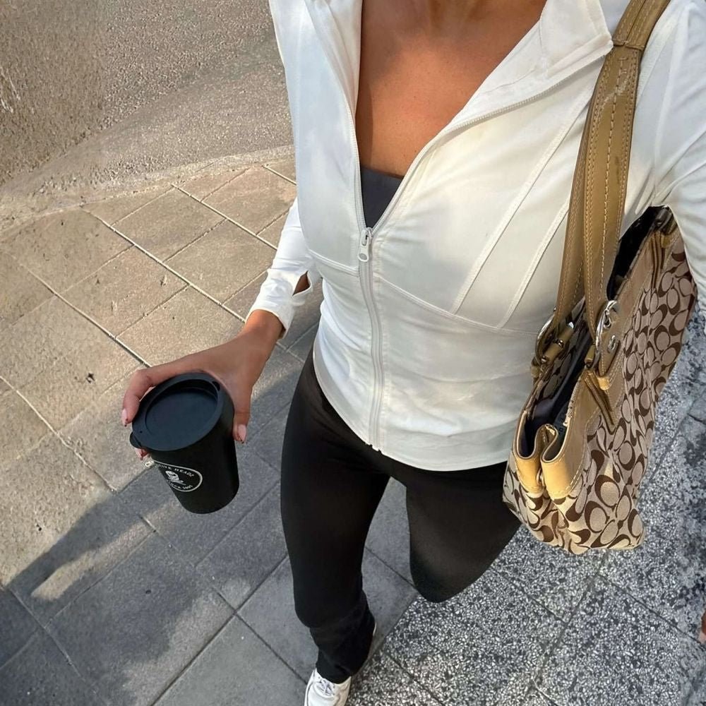 Model wearing the white Kouvr Sculpting Athletic Jacket in a modern fitness studio.