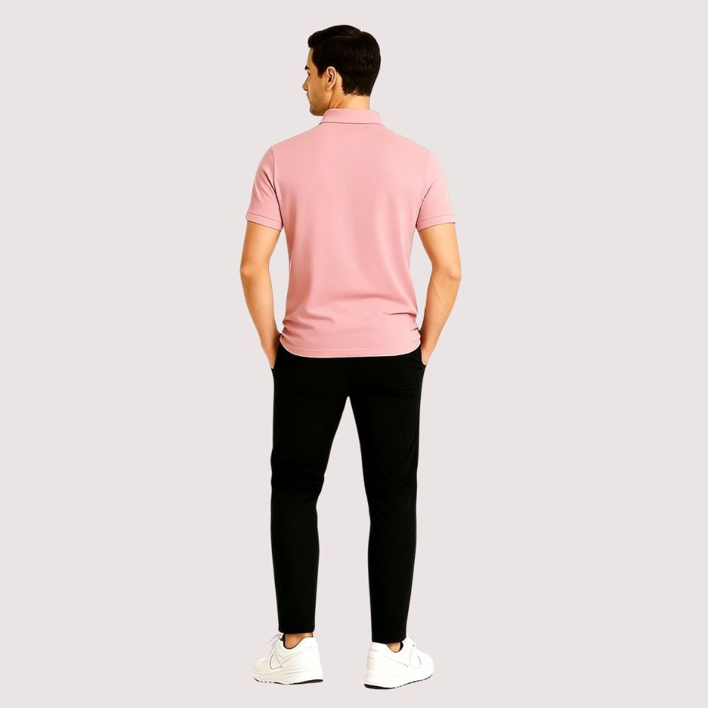 Man wearing a pink kouvr polo shirt and black pants on a light gray background