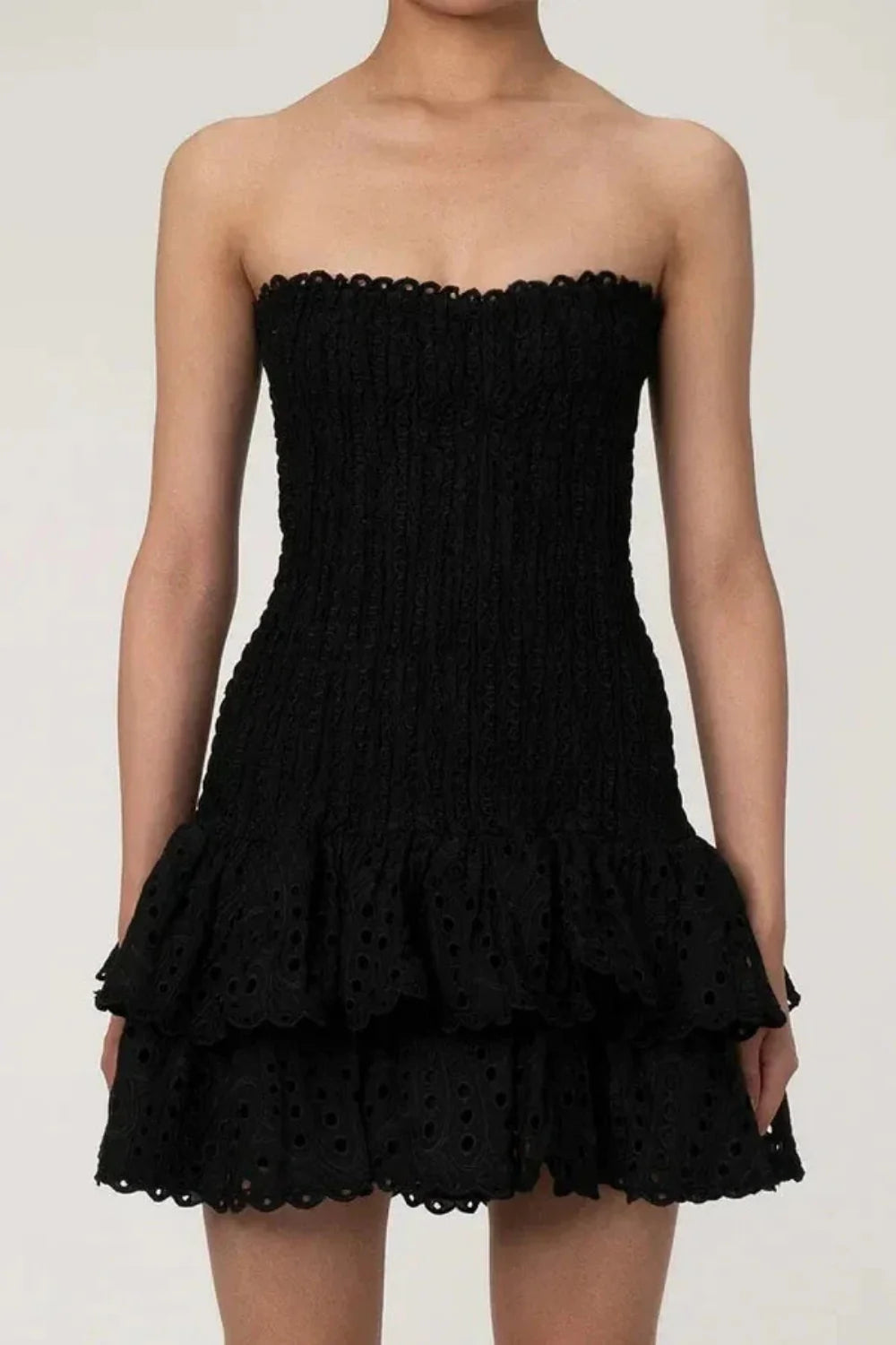Model wearing Kouvr Starla black strapless smocked mini dress with tiered eyelet skirt