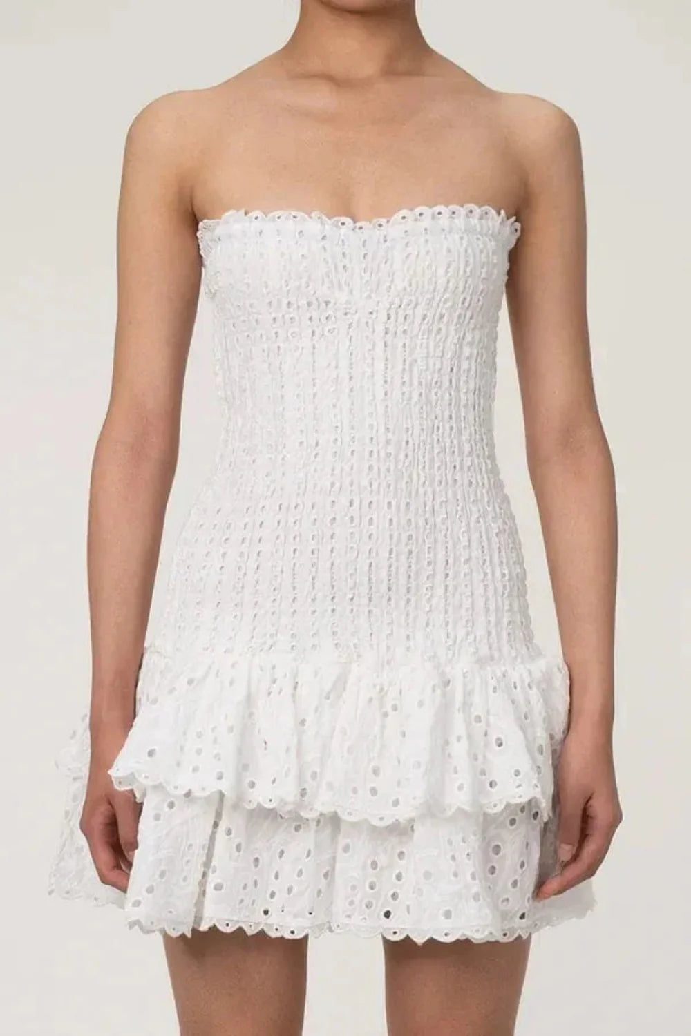 Model wearing the Kouvr Starla white strapless smocked mini dress with a tiered broderie anglaise ruffle skirt