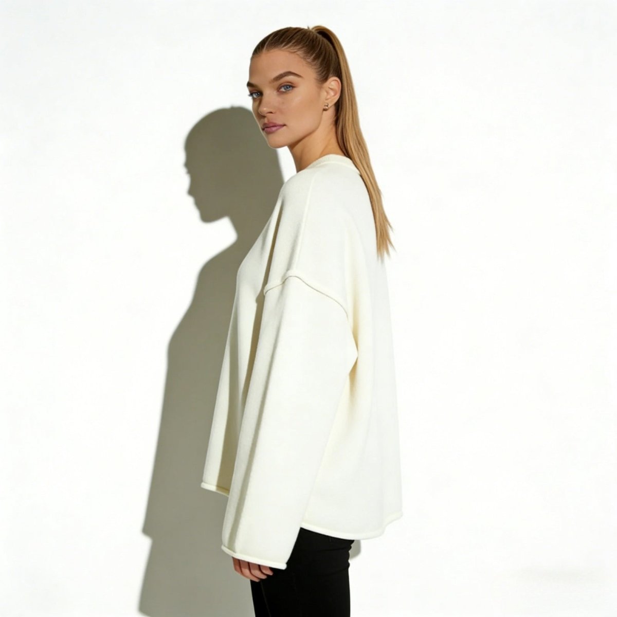 Side view of a woman in the Kouvr oversized ivory wool-blend sweater, showcasing the wide sleeve silhouette and modern dropped shoulder detail.
