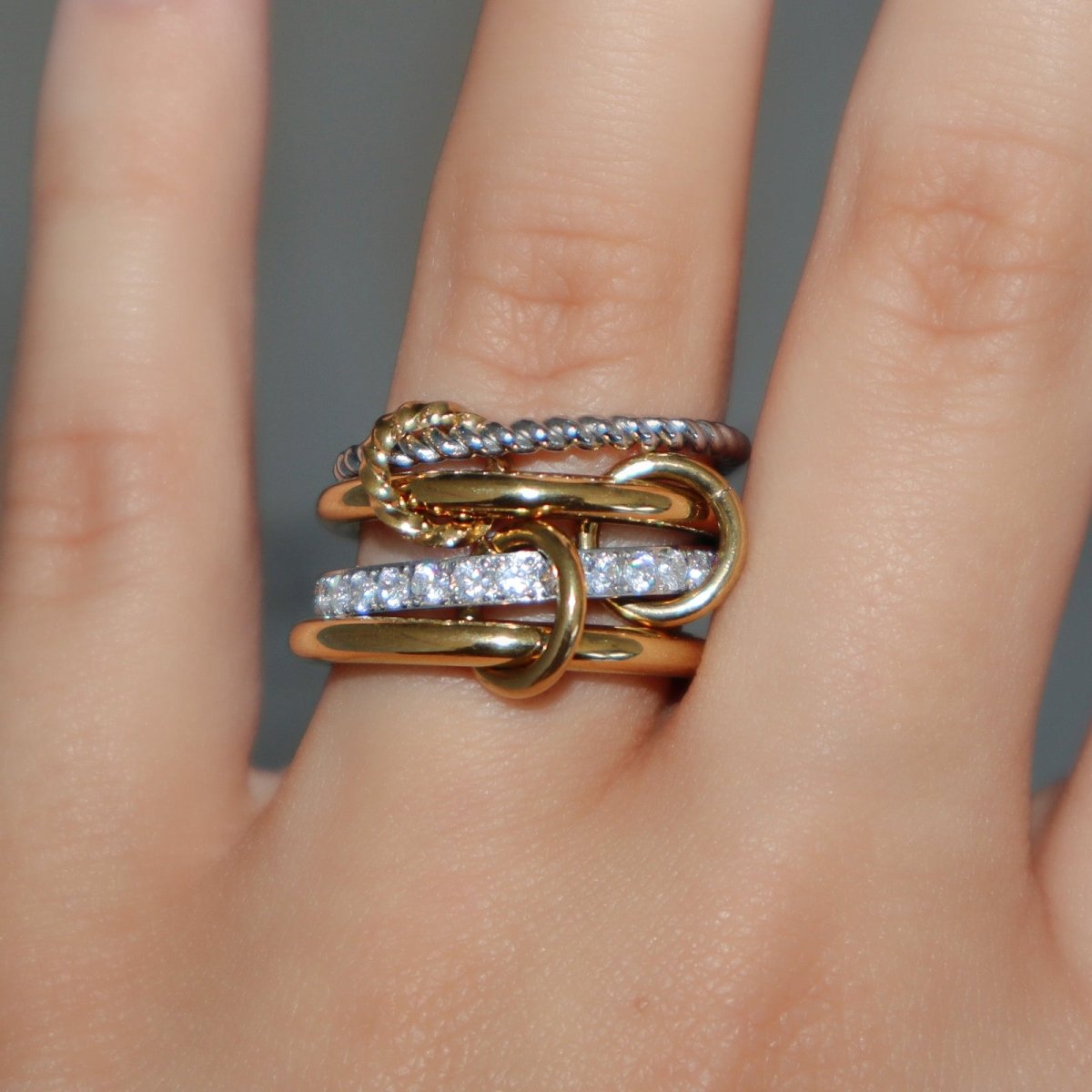 Kouvr Zeina interlocking stacked ring in 18k two-tone gold with pavé diamonds shown on a woman's finger.
