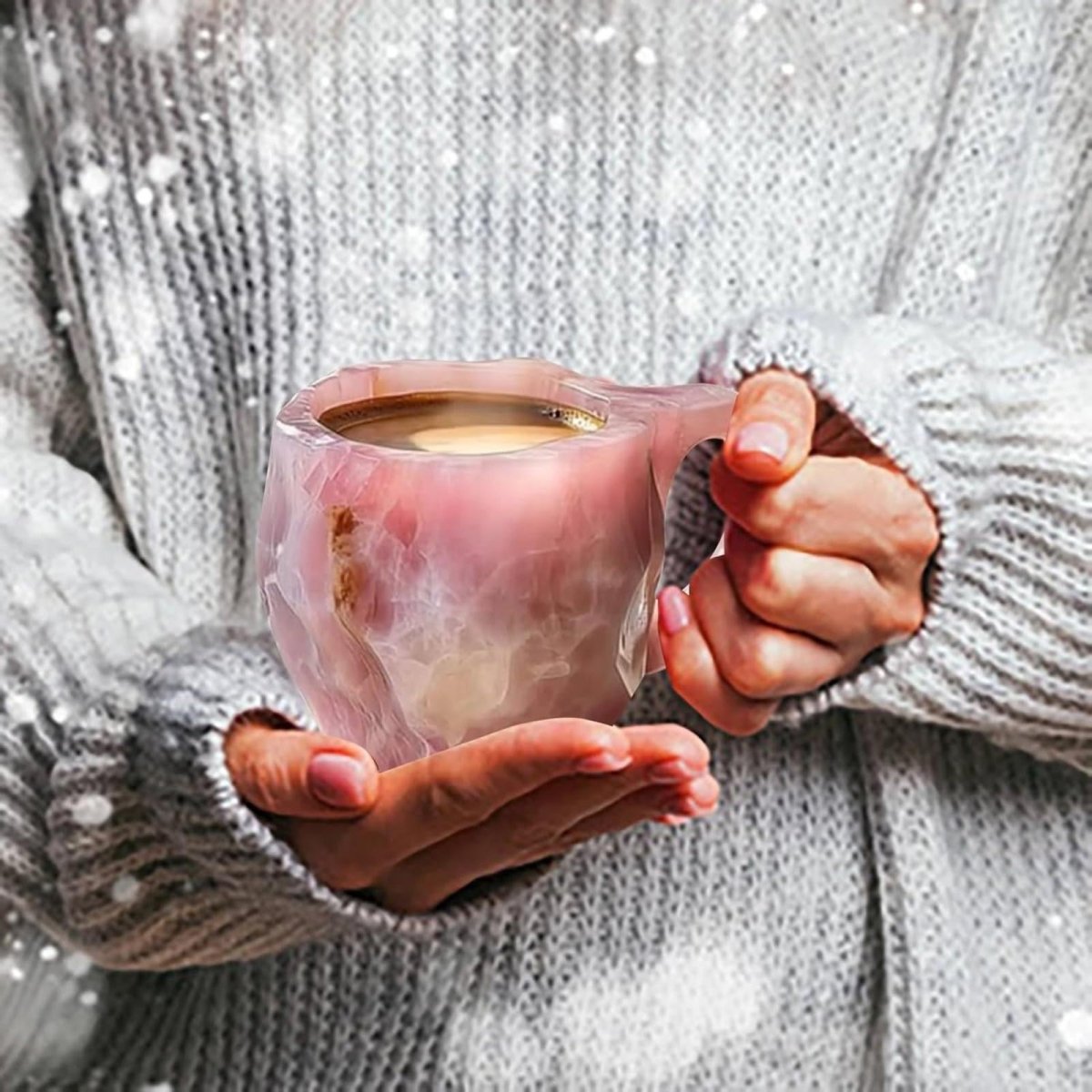 Close up of a woman's hands in a cozy white sweater holding a warm, steaming pink rose quartz coffee mug, conveying comfort and warmth.